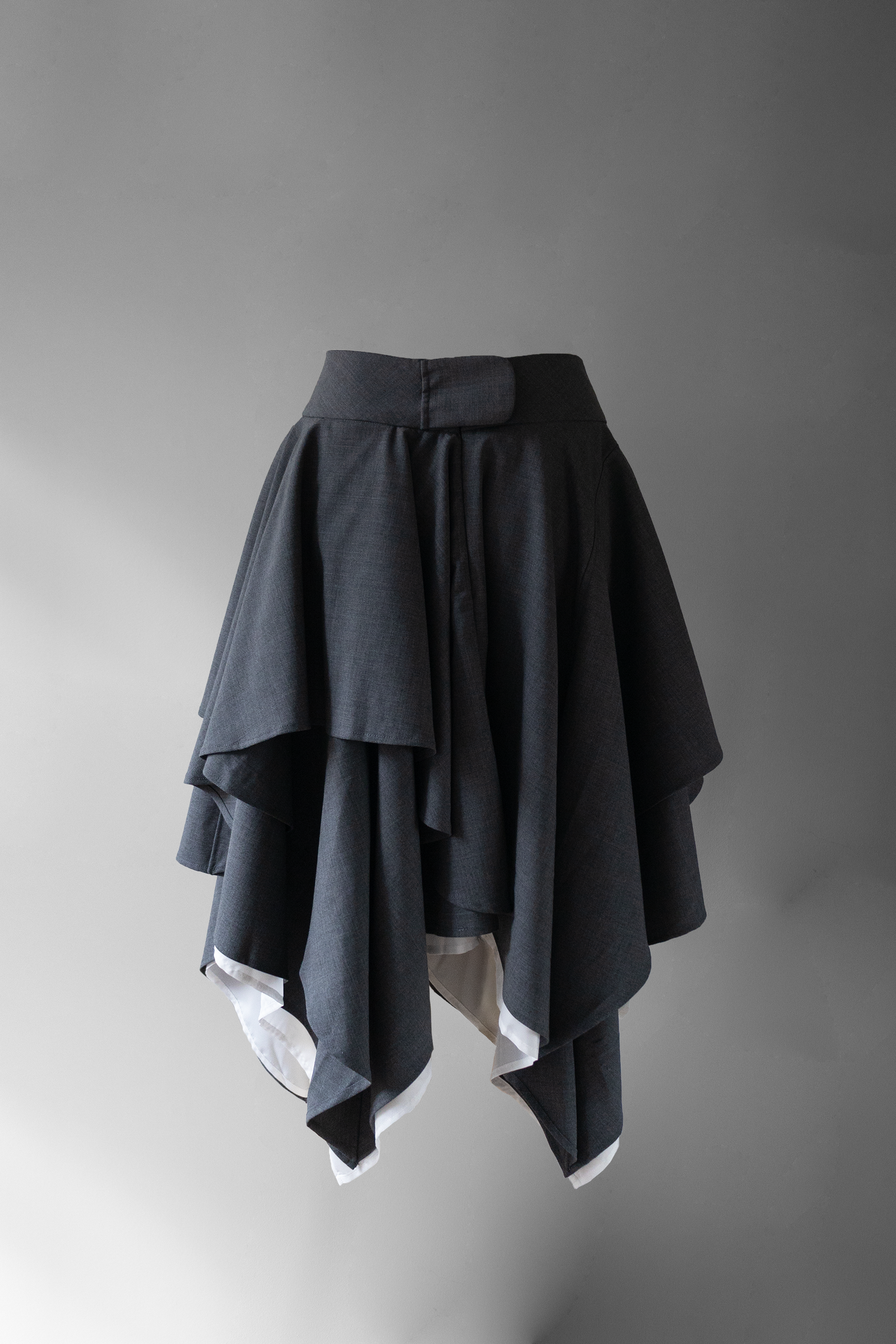back photo of the pixel skirt, a dark grey asymmetrical skirt with a large waistband and sheer white lining floating on a grey background.