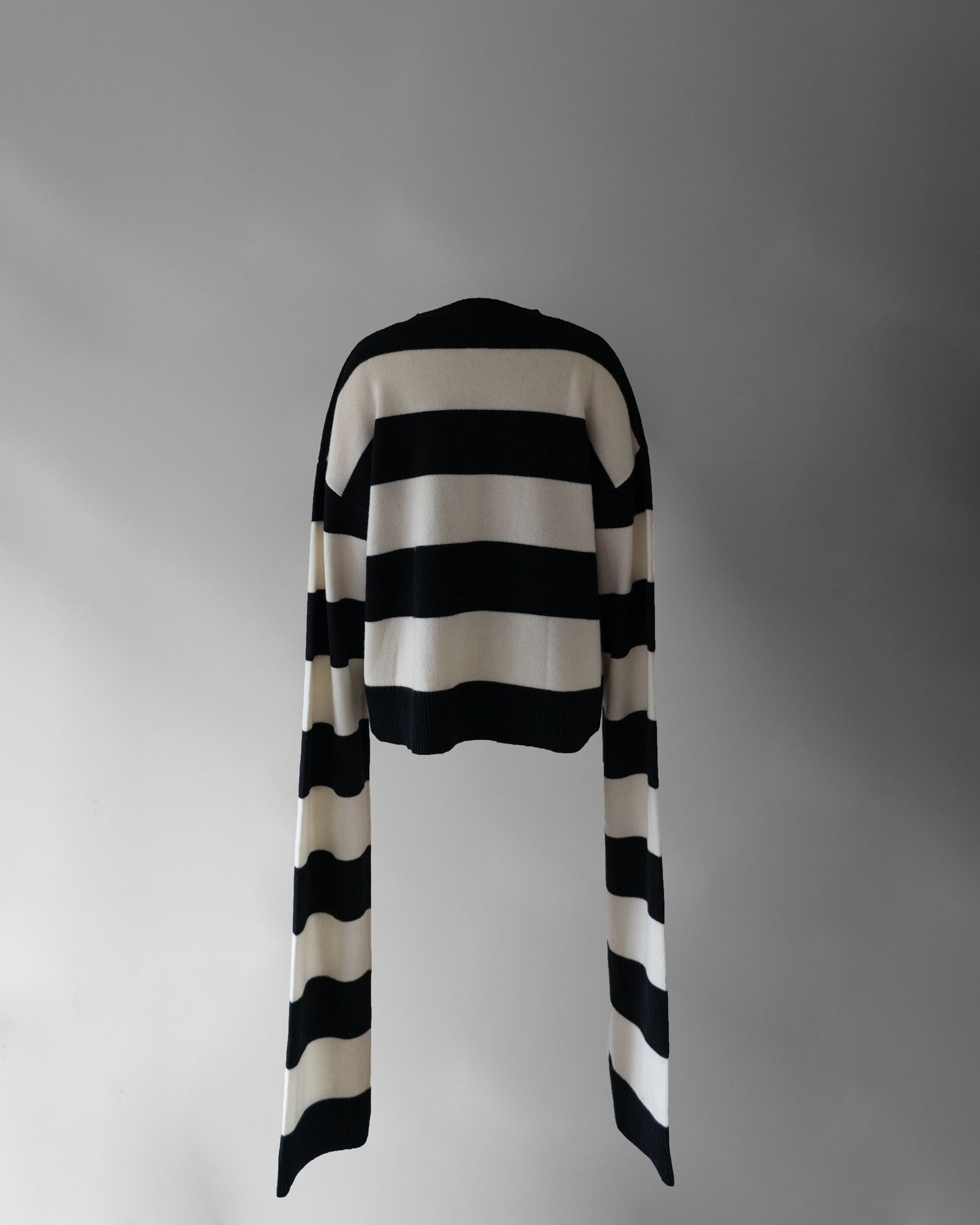 back photo of notebook sweater, a black and white striped sweater with very long sleeves floating on a light grey background.